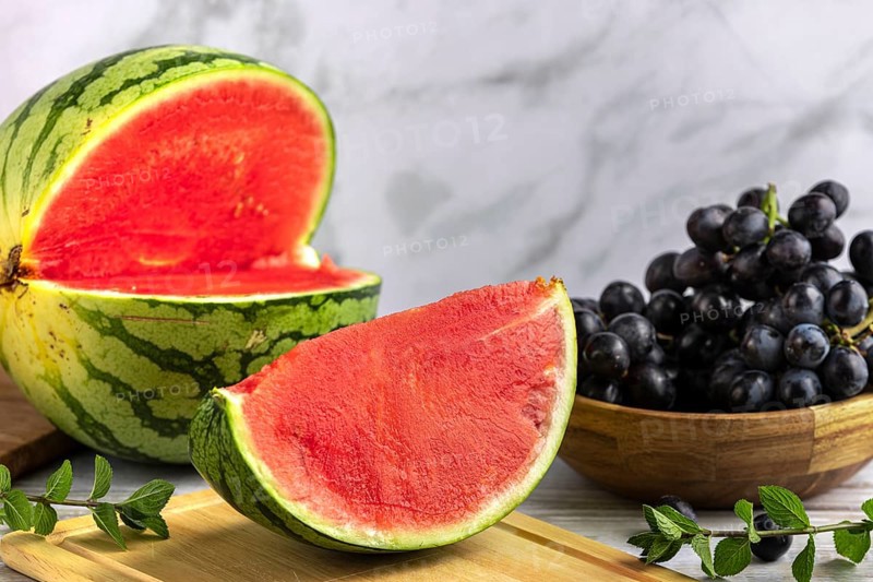 Sliced watermelon and grapes on a wooden board with mint leaves
