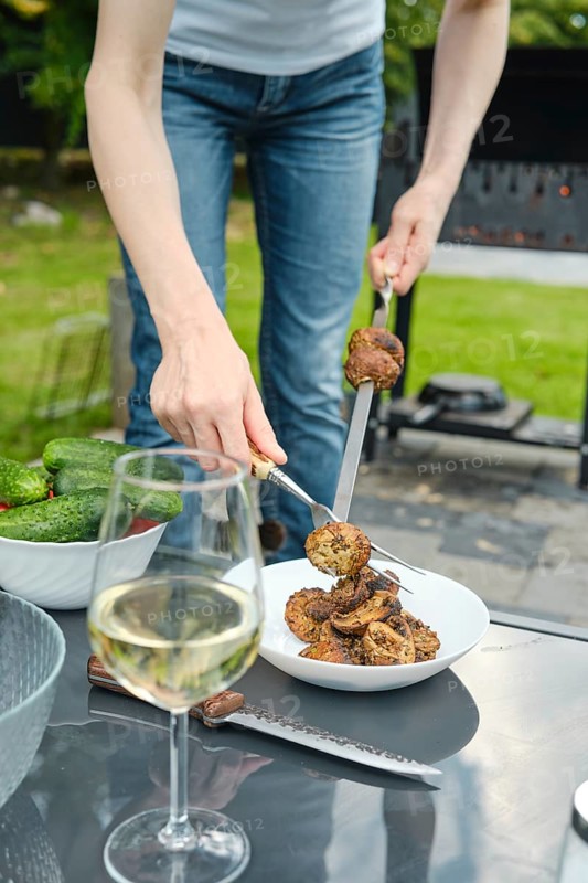Unrecognizable woman put grilled champignons in a plate with a fork