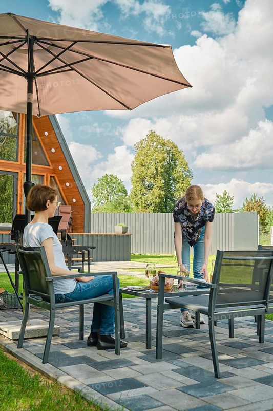 A young woman brought plates to the patio table to lay out grilled food on backyard