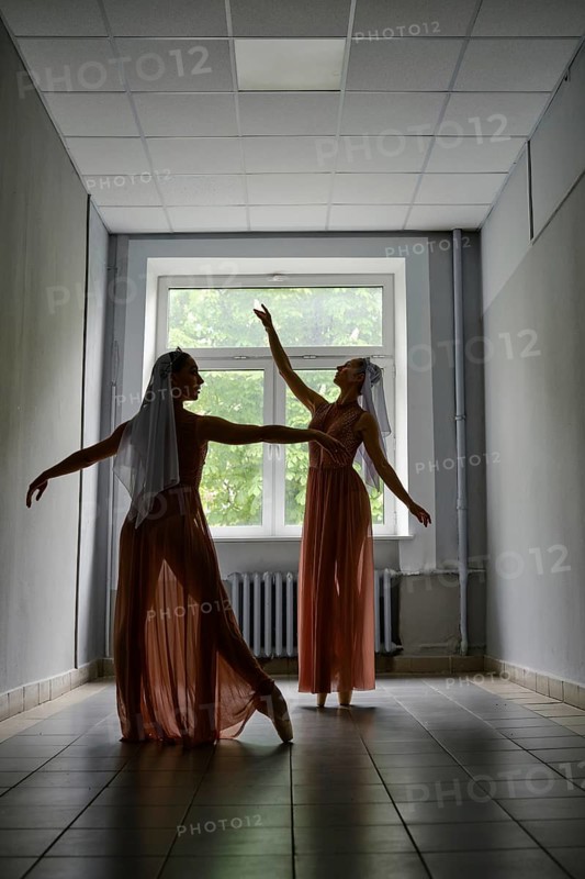 Silhouette of two dancers performing graceful artistic moves with their hands in corridor of theatre
