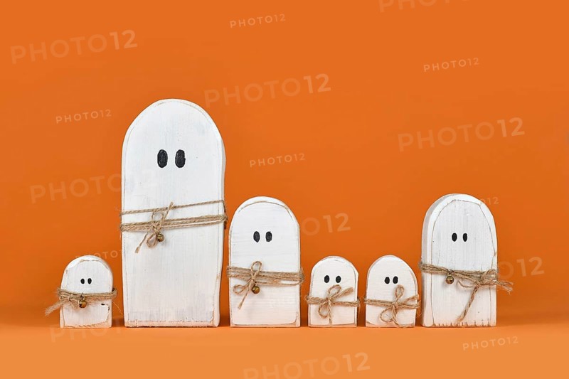 Cute wooden white Halloween ghost ornaments in a row on orange background