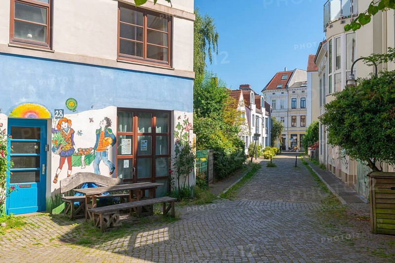 Residential street in the Ostertor neighbourhood a popular residential area, eastern suburb, Wilhelminian style building, traffic-calmed, graffiti, square with table and bench, green facades, farm shop, shop, cobblestones, sunshine, Bremen, Germany