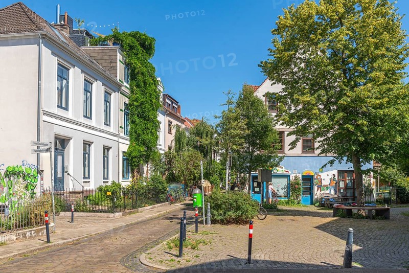 Residential street in the Ostertor neighbourhood a popular residential area, eastern suburb, Wilhelminian style buildings, traffic-calmed, graffiti, square with tree and bench, green facades, cobblestones, sunshine, Bremen, Germany