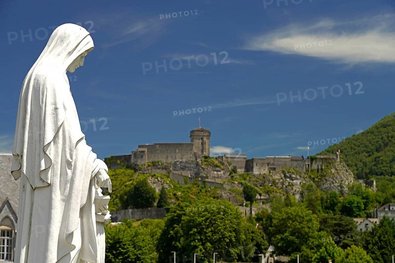 Statue on Rosary Square and the ChÃ¢teau fort de Lourdes fortress in the Marian pilgrimage town of Lourdes, Pyrenees, France