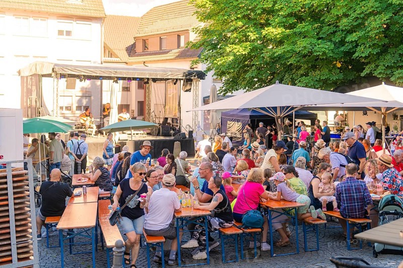 Visitors sit at beer tables at an open-air concert, surrounded by trees and parasols, 950 years Weil der Stadt ceremony, Böblingen district, Germany
