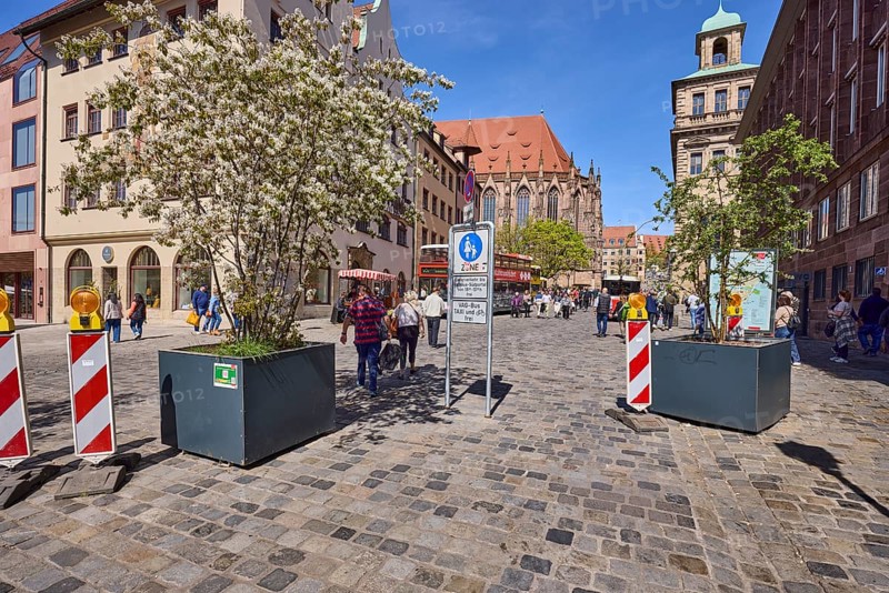 Pedestrian zone, barrier beacons, flower pots, blossoming tree, Canadian rock pear (Amelanchier canadensis), pavement made of cobblestones, historical buildings, church, pedestrians as secondary motif, blue sky, intersection main market with Waaggasse, Nuremberg, Middle Franconia, independent city, Bavaria, Germany