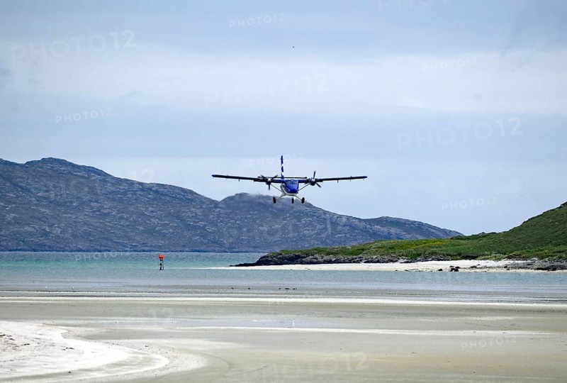 An aeroplane lands on a runway on the beach with mountains in the background and a calm atmosphere, Outer Hebrides, Isle of Barra, Scotland, United Kingdom