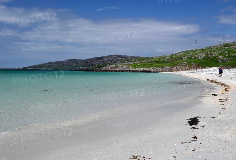 Clear bright blue beach with gentle waves under a cloudless sky, two people at the water's edge, Outer Hebrides, Eriksay, Scotland, United Kingdom