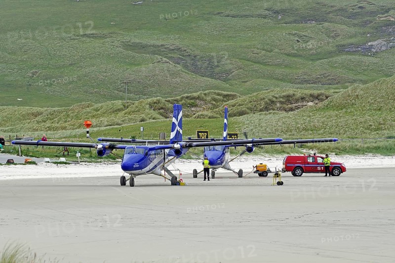 Aeroplanes standing on a runway in front of green hills, accompanied by a red vehicle, Outer Hebrides, Isle of Barra, Scotland, United Kingdom