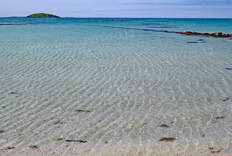 Clear bright blue beach with gentle waves under a cloudless sky, Outer Hebrides, Eriksay, Scotland, United Kingdom