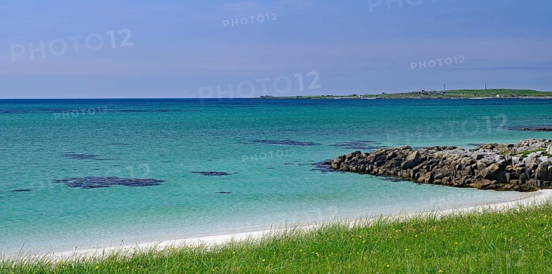 Clear blue sky over a rocky coastline with green grass and blue water, Outer Hebrides, South Uist, Scotland, United Kingdom