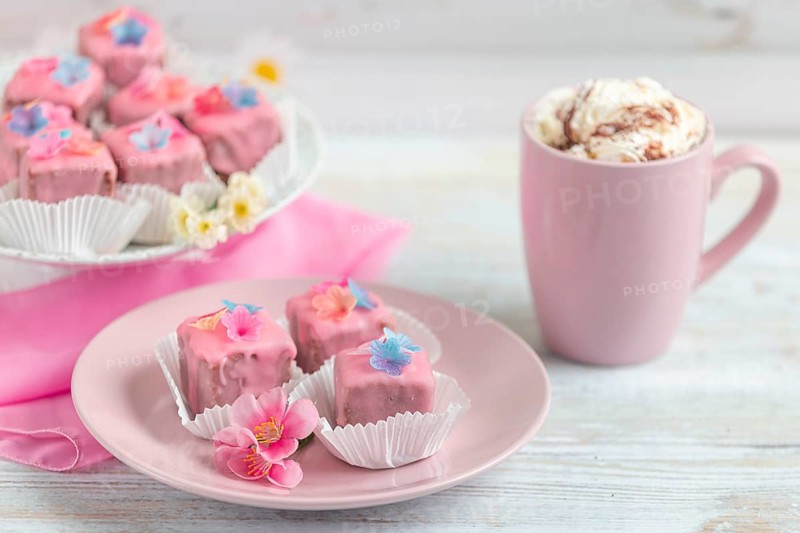 Pink petit fours and a cup of coffee with cream on a table