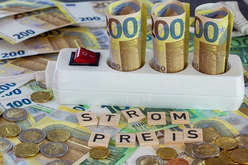Symbolic image of electricity costs: multiple socket with euro banknotes and euro coins, with the word STROMPREIS in wooden letters in front of it