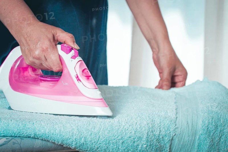 Ironing clothes at home, in a bright room, with natural light, female hands