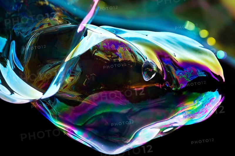 Irregular, iridescent soap bubble in the colours of the rainbow against a black background, Recklinghausen, Germany