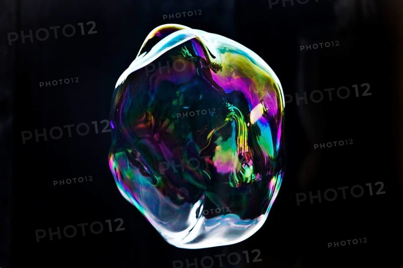 A large iridescent and floating soap bubble in the colours of the rainbow against a black background, Recklinghausen, Germany