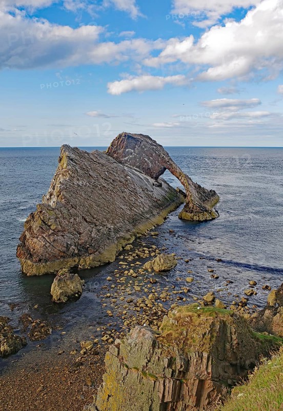 Remarkable rock formation jutting into the sea under a blue sky with few clouds, Bow Fiddle Rock, Aberdeenshire, Buckie, Scotland, United Kingdom