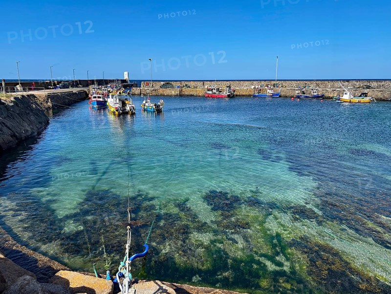 Clear water view of a harbour with small boats surrounded by a stone quay wall, Aberdeenshire, Scotland, United Kingdom