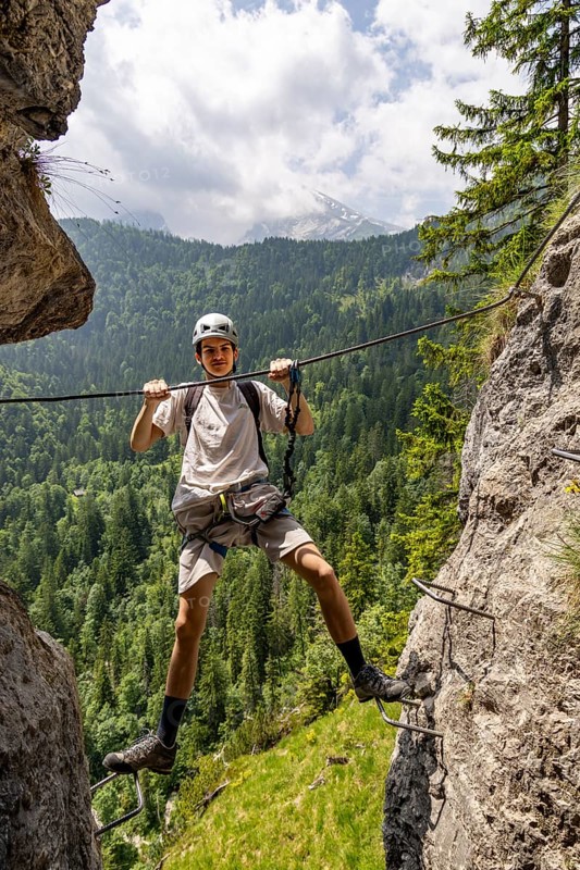 Mountaineer climbing over a steep gorge in the Isidor via ferrata, GrÃ¼nstein, Watzmann in the background, Schönau am Königssee, Berchtesgadener Land, Upper Bavaria, Bavaria, Germany