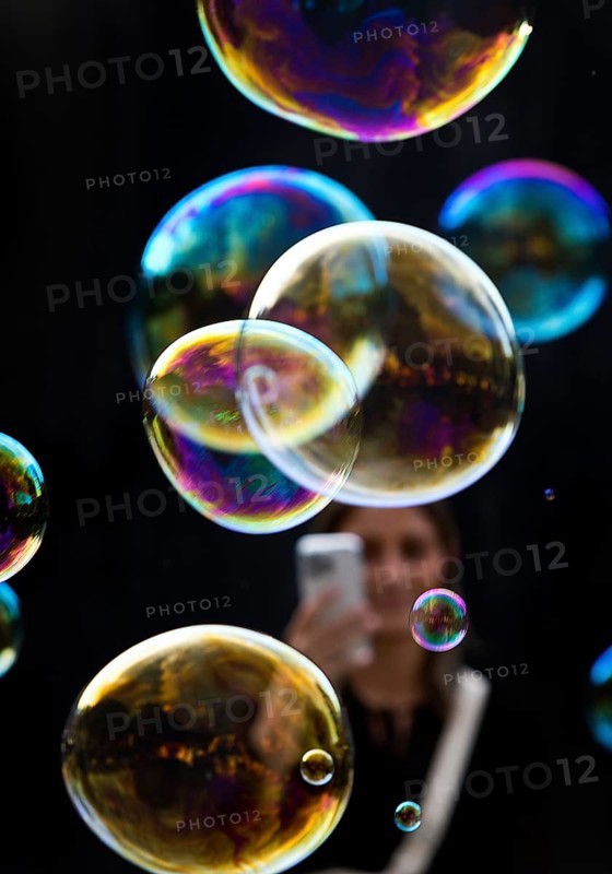 A woman photographs shimmering and floating soap bubbles against a black background, Recklinghausen, North Rhine-Westphalia, Germany