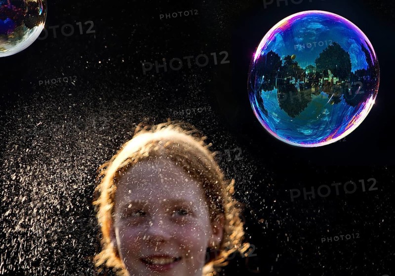 A girl is happy about a shimmering and floating soap bubble in front of a black background, Recklinghausen, Germany