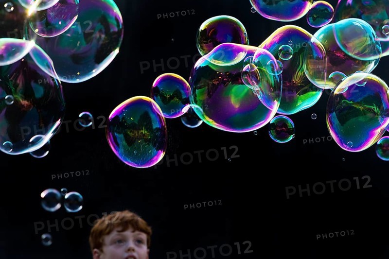 A boy marvels at shimmering and floating soap bubbles against a black background, Recklinghausen, Germany