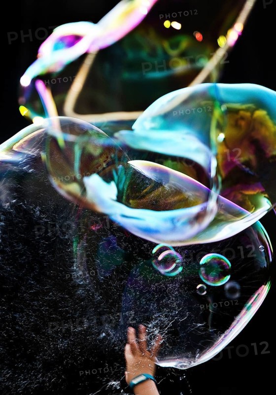 A hand bursts a large iridescent soap bubble against a black background, Recklinghausen, Germany