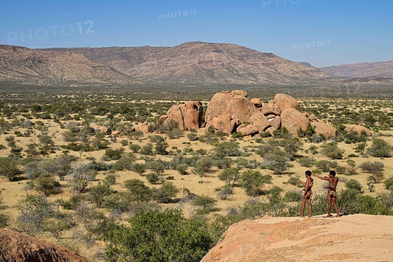 Two Bushmen with bows and arrows overlooking the landscape from a rocky hill, Erongo Mountains, Namibia