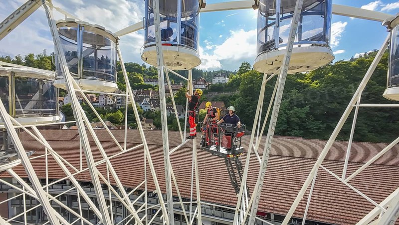 Workers in a Ferris wheel with lifting platform, surrounded by green hills and blue sky, fire brigade exercise for gondola rescue, Germany