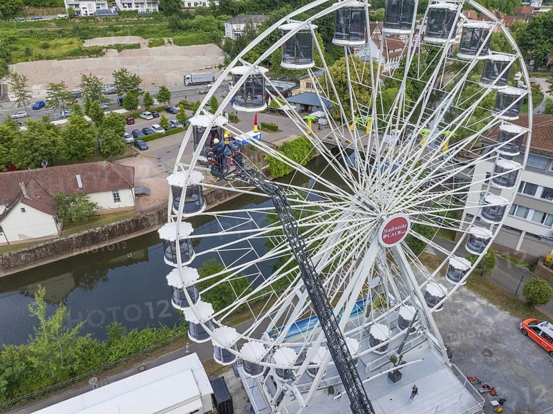 Aerial view of a Ferris wheel next to a river with cars on the road and trees in the background, fire brigade exercise for gondola rescue, Germany
