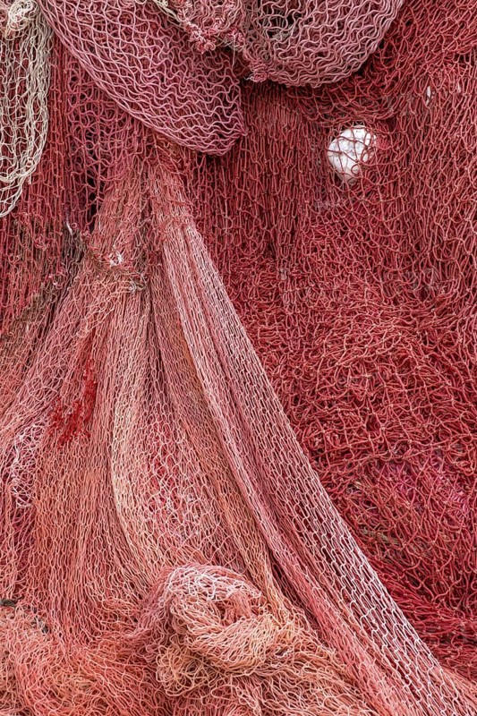 Colourful fishing nets in shades of red that create an interwoven, textured surface, Croatia