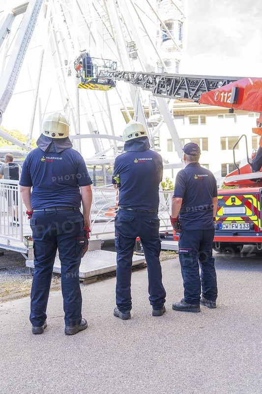 Three firefighters in uniforms standing in front of emergency vehicle with lifting platform, fire brigade exercise for gondola rescue Ferris wheel, Calw, Germany
