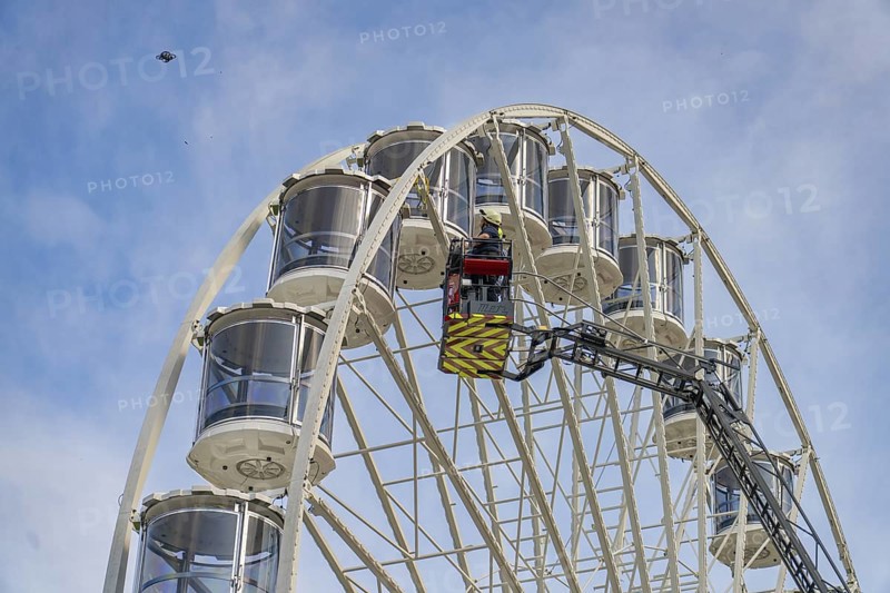 Firefighter in the rescue cage near the cabins of the Ferris wheel in front of a blue sky, fire brigade exercise for gondola rescue Ferris wheel, Calw, Germany