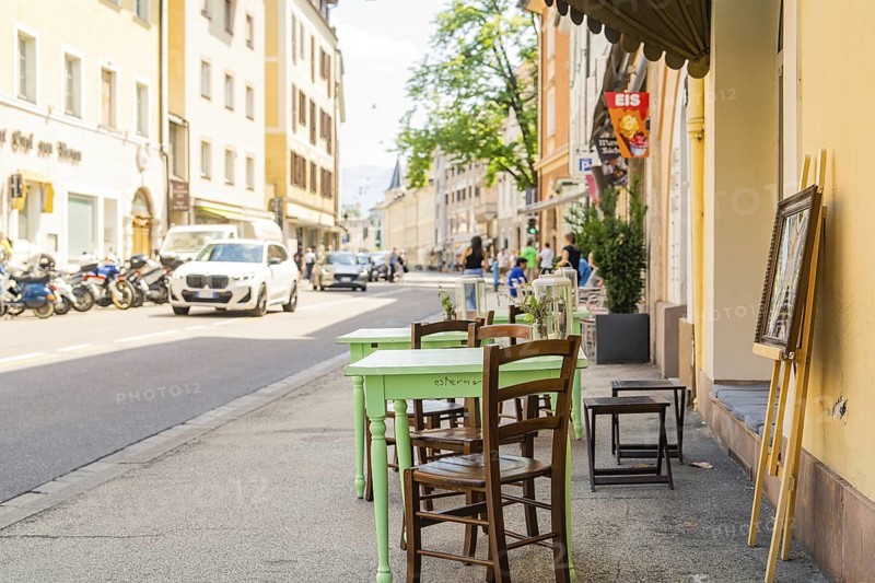 A street café with green wooden chairs in sunny weather in a lively town, Merano, South Tyrol, Italy