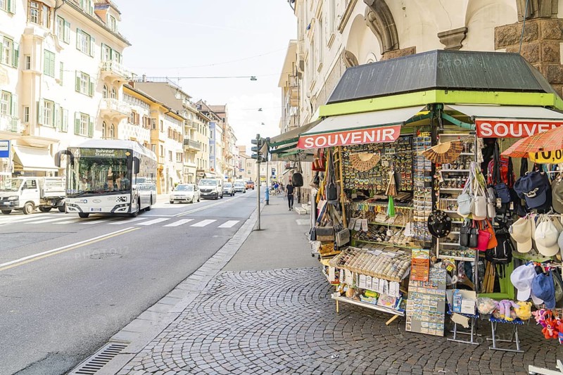 A souvenir stand on the pavement near a busy street with a passing bus, Merano, South Tyrol, Italy