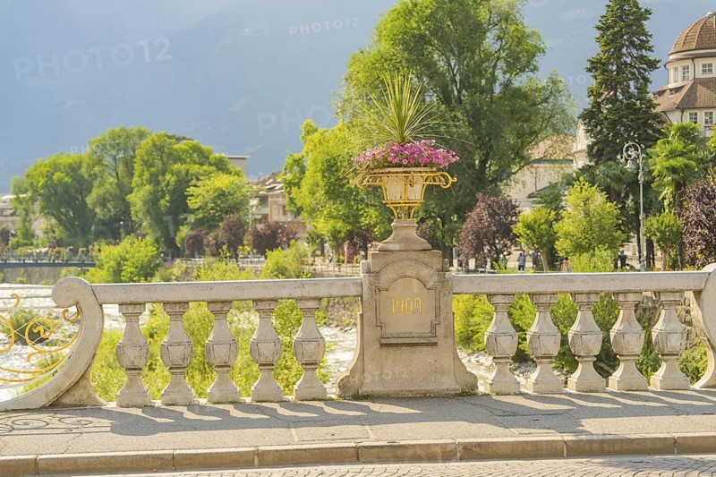 Decorative stone bridge with flower pot on the riverbank on a sunny day, Merano, South Tyrol, Italy