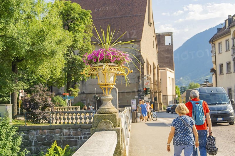 A couple walks across the stone bridge, view of mountains and flowers, Merano, South Tyrol, Italy
