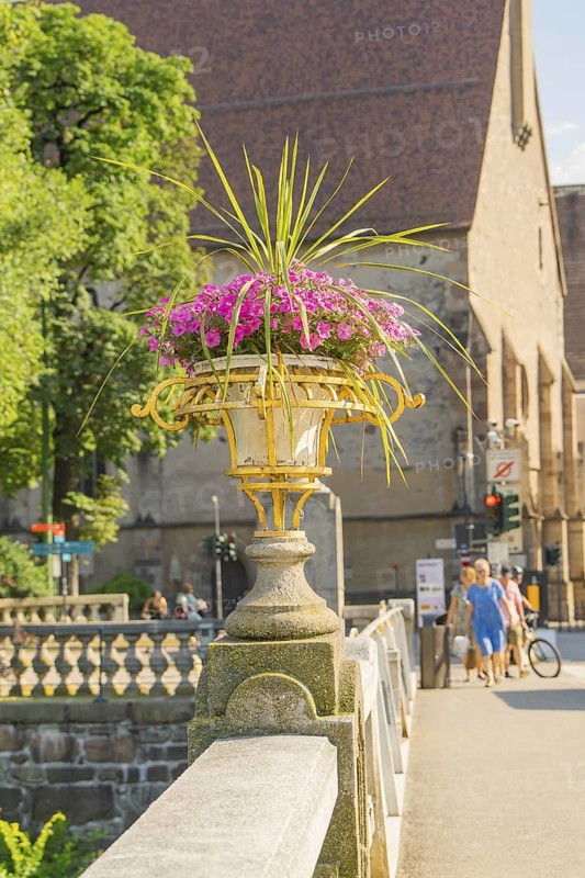 Stone bridge with flower pot, church and pedestrians in the background, Merano, South Tyrol, Italy