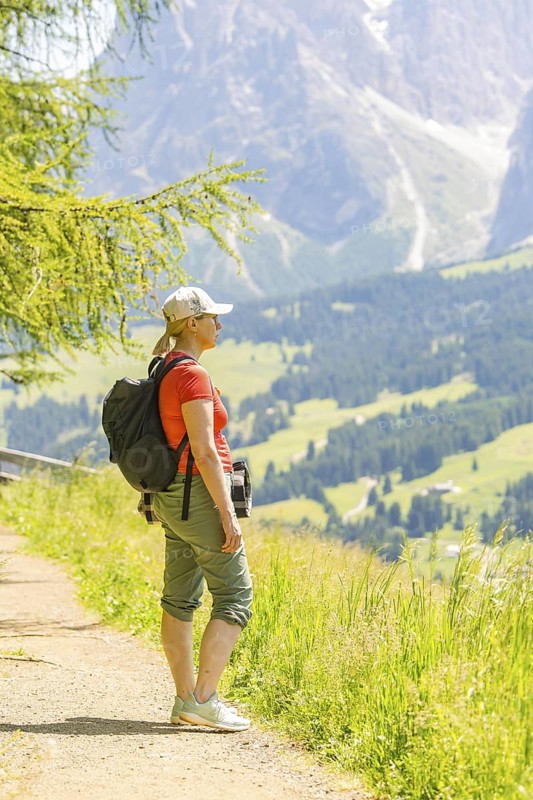 Woman in hiking clothes looking at the mountain landscape from a sunny path, Alpe di Siusi, Dolomites, South Tyrol, Italy