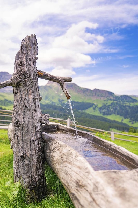A rustic wooden fountain with running water in a picturesque mountain landscape, Zallinger Alm, Dolomites, Italy