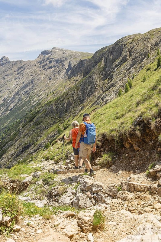 Two hikers on a stony path with a wide view over a mountain landscape, Schlehrn hike, Alpe di Siusi, Dolomites, South Tyrol, Italy