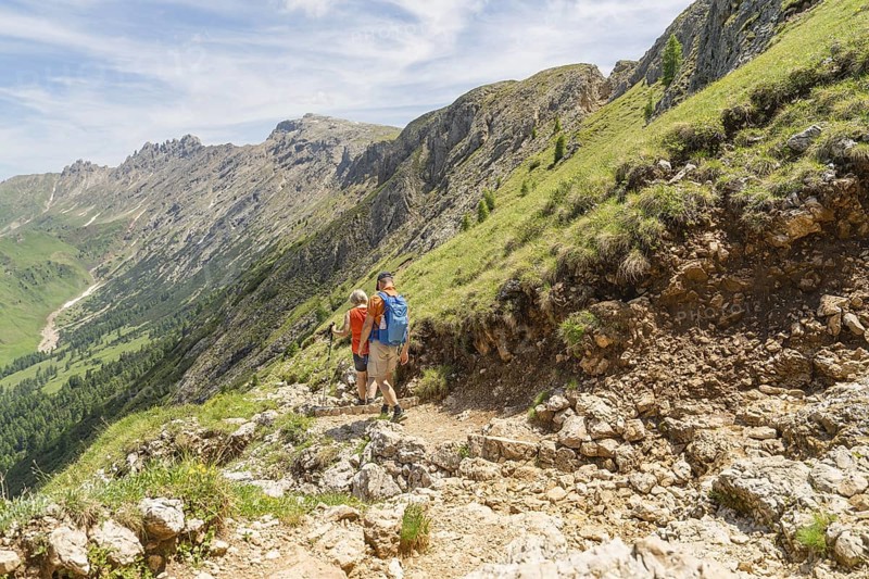 Hikers on a mountainous path with green meadows and stony ground under a blue sky, Schlehrn hike, Seiser Alm, Dolomites, South Tyrol, Italy
