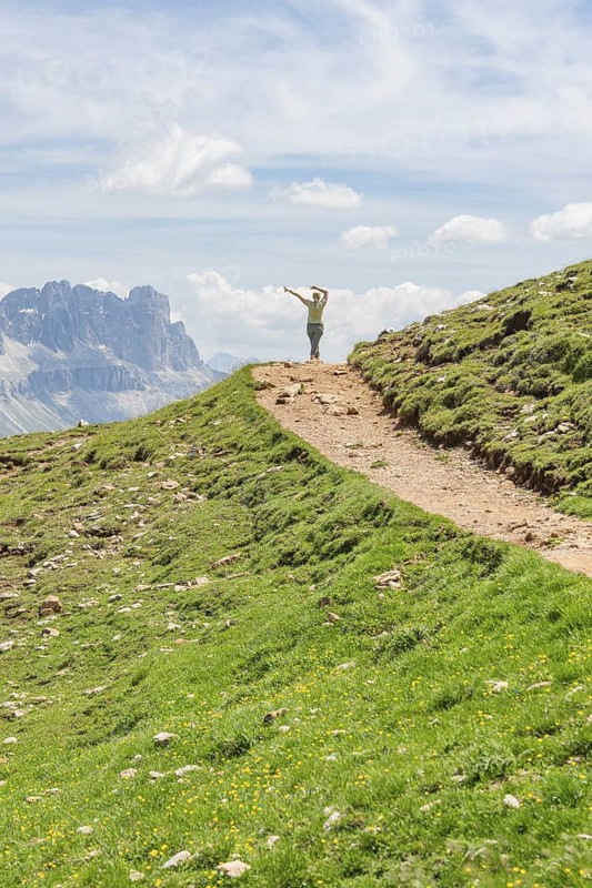 Person hiking on a path with views of rocky mountains and wide skies, Schlehrn hike, Alpe di Siusi, Dolomites, South Tyrol, Italy