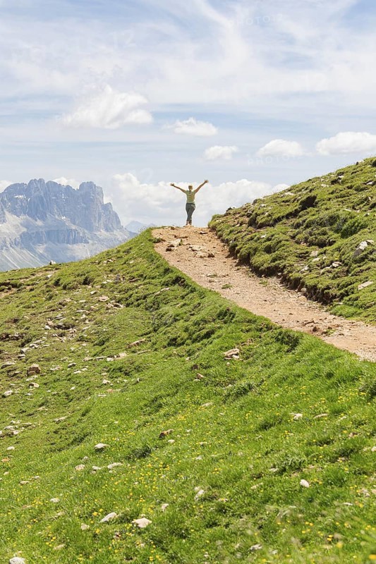 Person opens his arms on a hill path with a view of rocky mountains, Schlehrn hike, Alpe di Siusi, Dolomites, South Tyrol, Italy