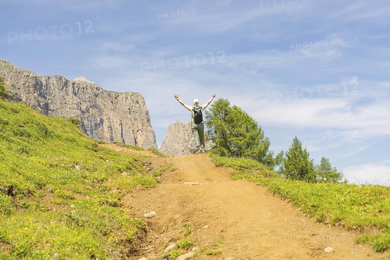 A hiker enjoys a sunny path in a mountainous landscape, Schlehrn hike, Alpe di Siusi, Dolomites, South Tyrol, Italy