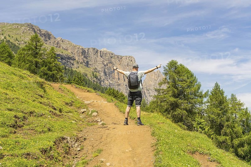 A hiker with outstretched arms on a mountain path, surrounded by green nature, Schlehrn hike, Alpe di Siusi, Dolomites, South Tyrol, Italy