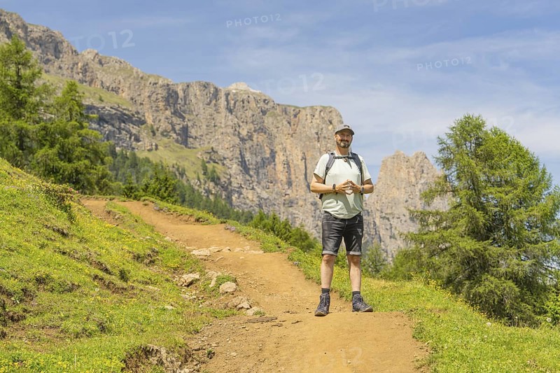 A hiker with a rucksack on a path against a rocky mountain backdrop in fine weather, Schlehrn hike, Alpe di Siusi, Dolomites, South Tyrol, Italy