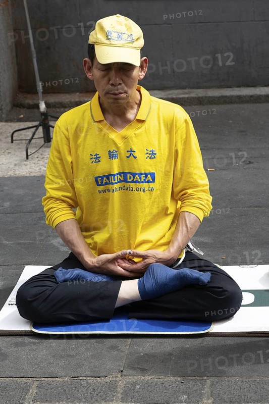Falun Dafa or Falun Gong man meditating sitting cross legged, Gerrard Street, Chinatown, West End, London, England, UK