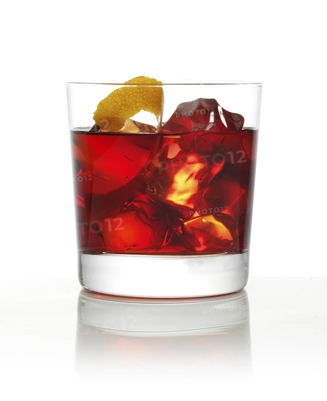 Cocktail in a tumbler on ice with an orange zest as garnish against a white background, studio shot