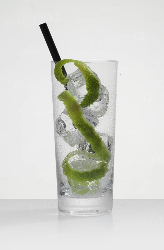 Betautes cocktail glass, filled with ice cube cubes, lime zest as garnish, in front of a white background, studio shot